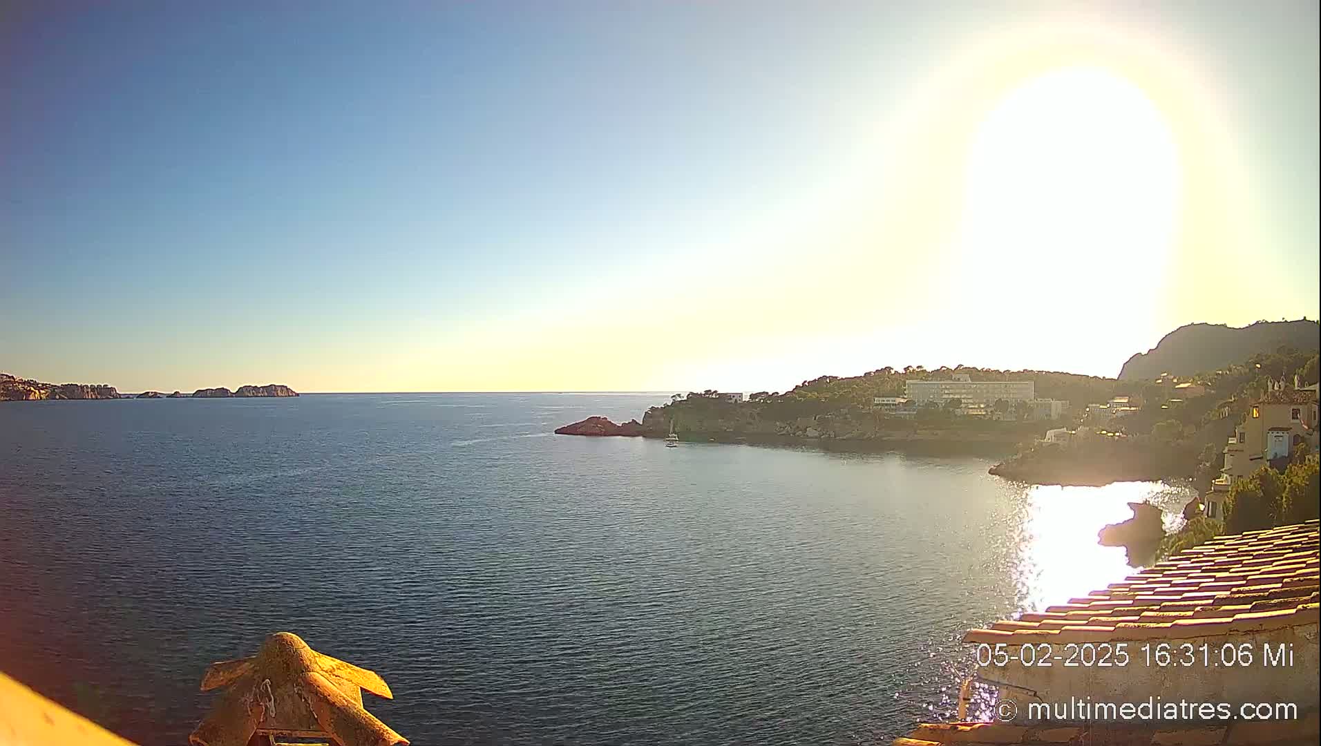 A bright, sunny day reveals a calm sea with a coastal town and distant islands under a clear blue sky.
