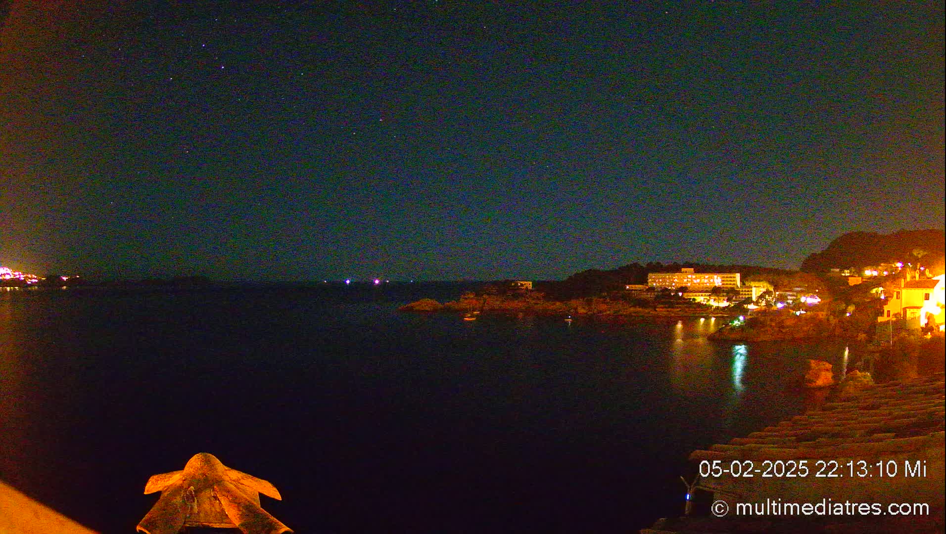 A nighttime view of a dark body of water with illuminated buildings and a starry sky above.