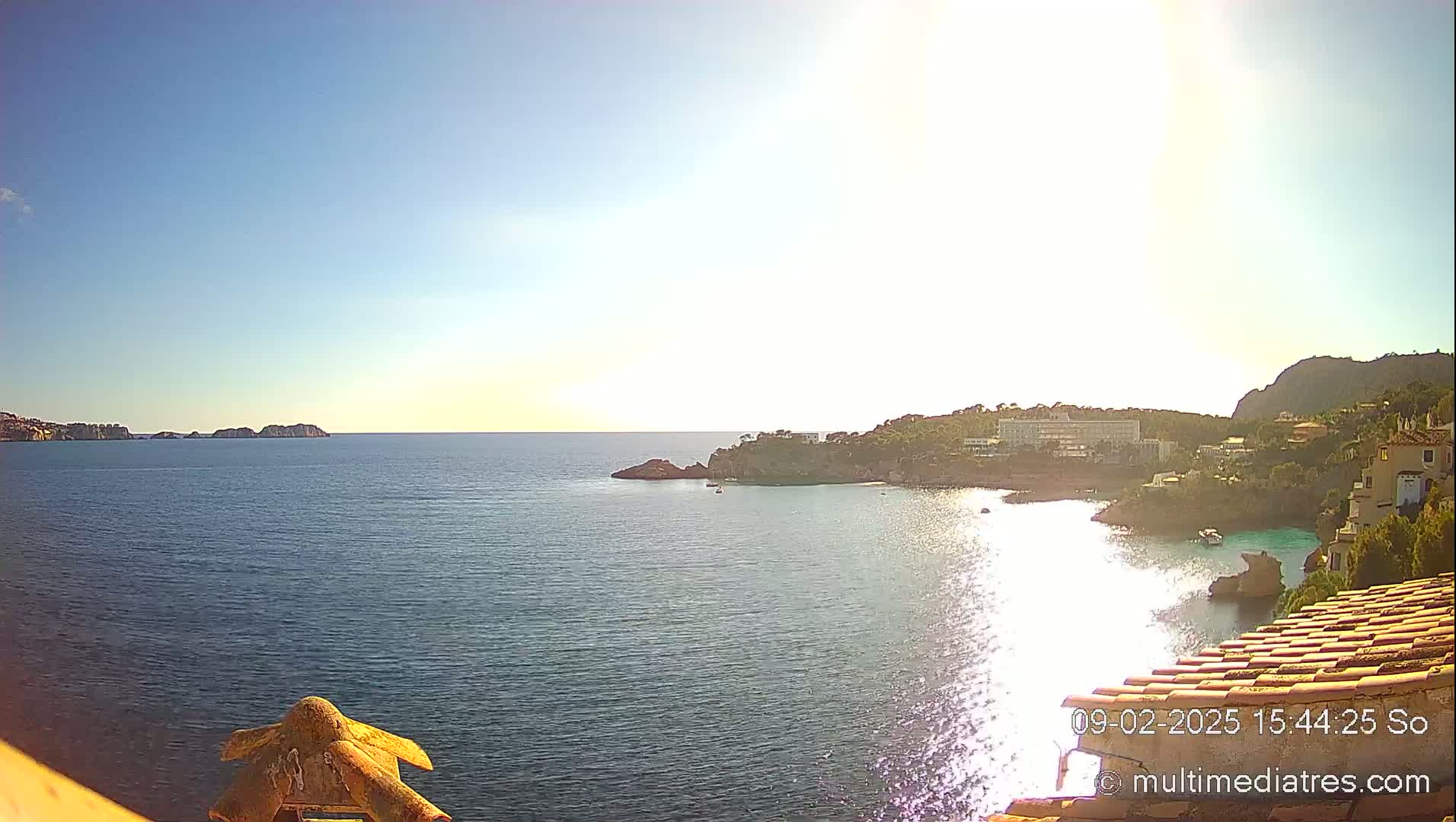 A sunny, bright day overlooks a calm, blue ocean bay with a town nestled into the rocky coastline.