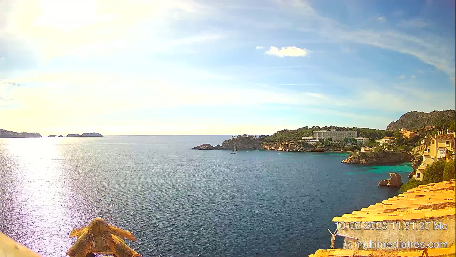 A sunny day overlooking a calm ocean bay with a hotel and buildings on a rocky coastline.