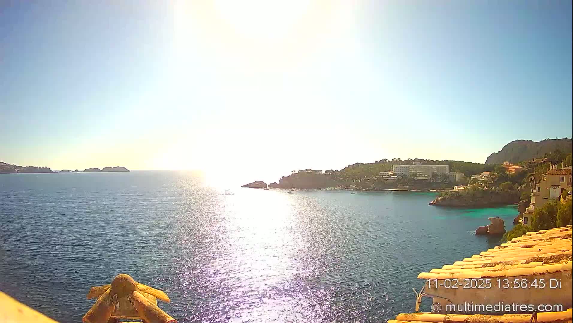 A sunny, bright day overlooking a calm sea with a coastline featuring buildings and rocky outcrops.