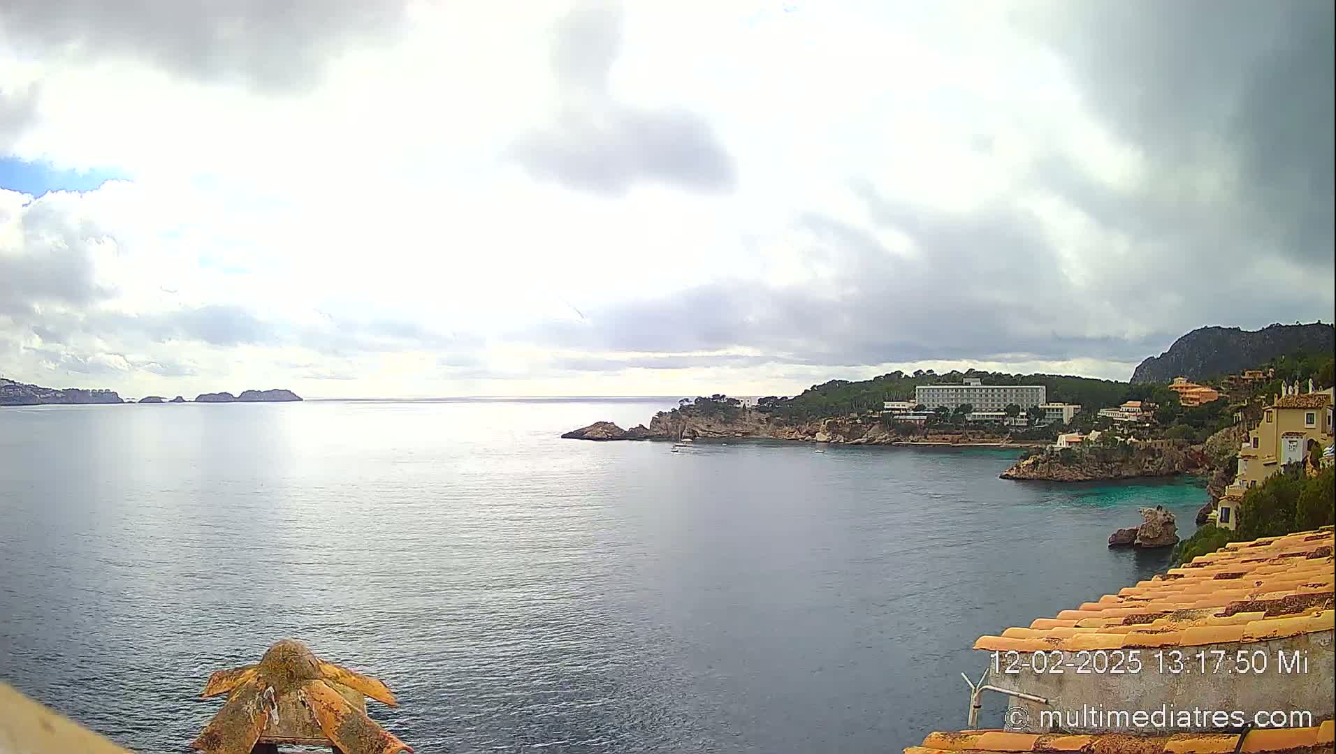 A partly cloudy day overlooks a calm bay with a hotel and residential buildings nestled into the coastline, and small islands visible in the distance.
