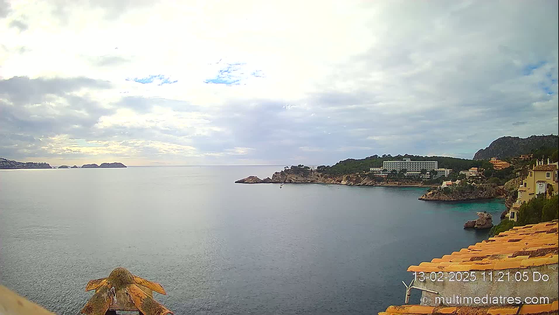 A calm sea stretches out under a cloudy sky, encompassing a coastline with buildings and a prominent hotel nestled into rocky cliffs.