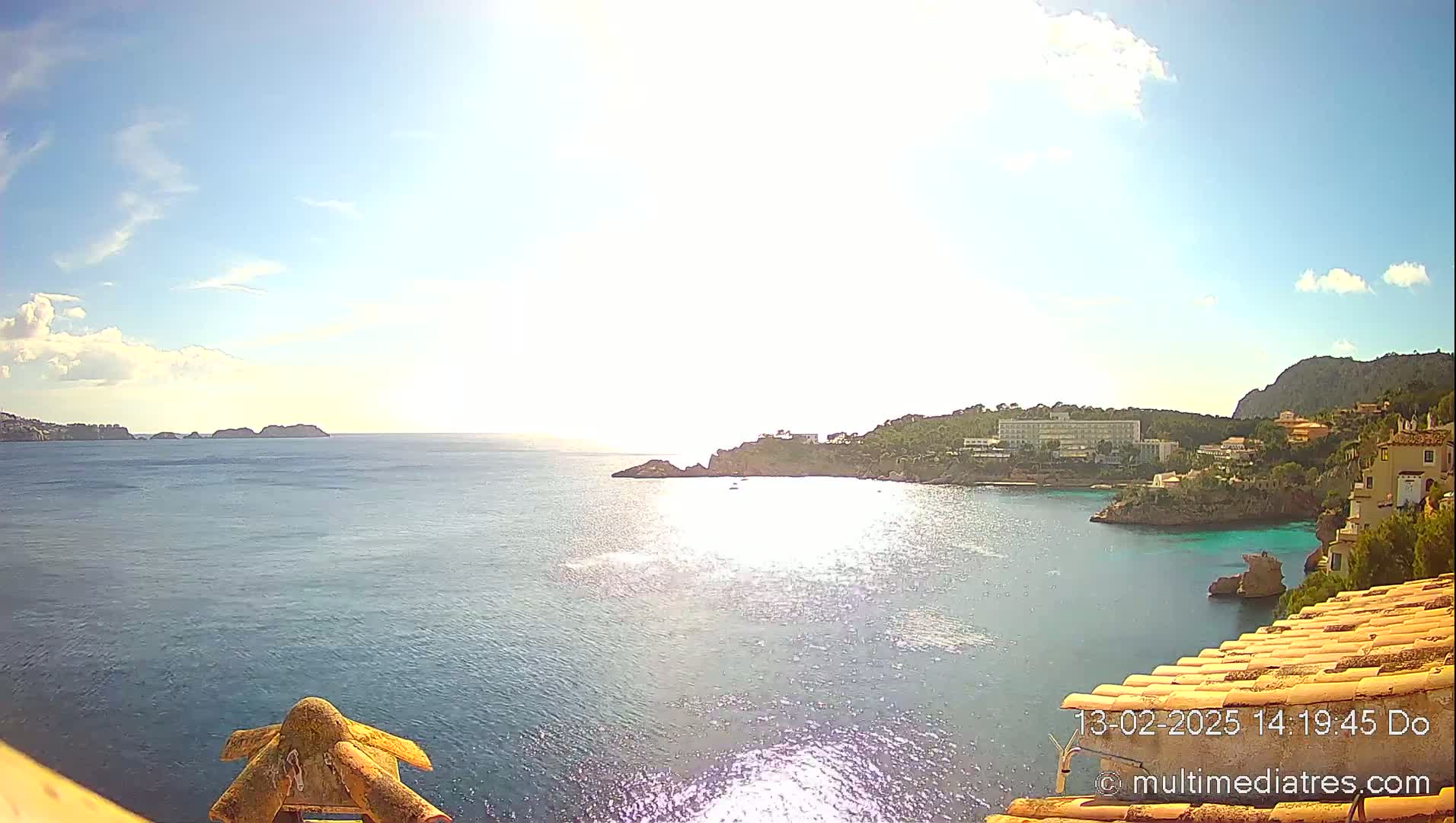 A sunny day reveals a picturesque coastal scene with a calm sea, rocky inlets, and buildings nestled along the shoreline.