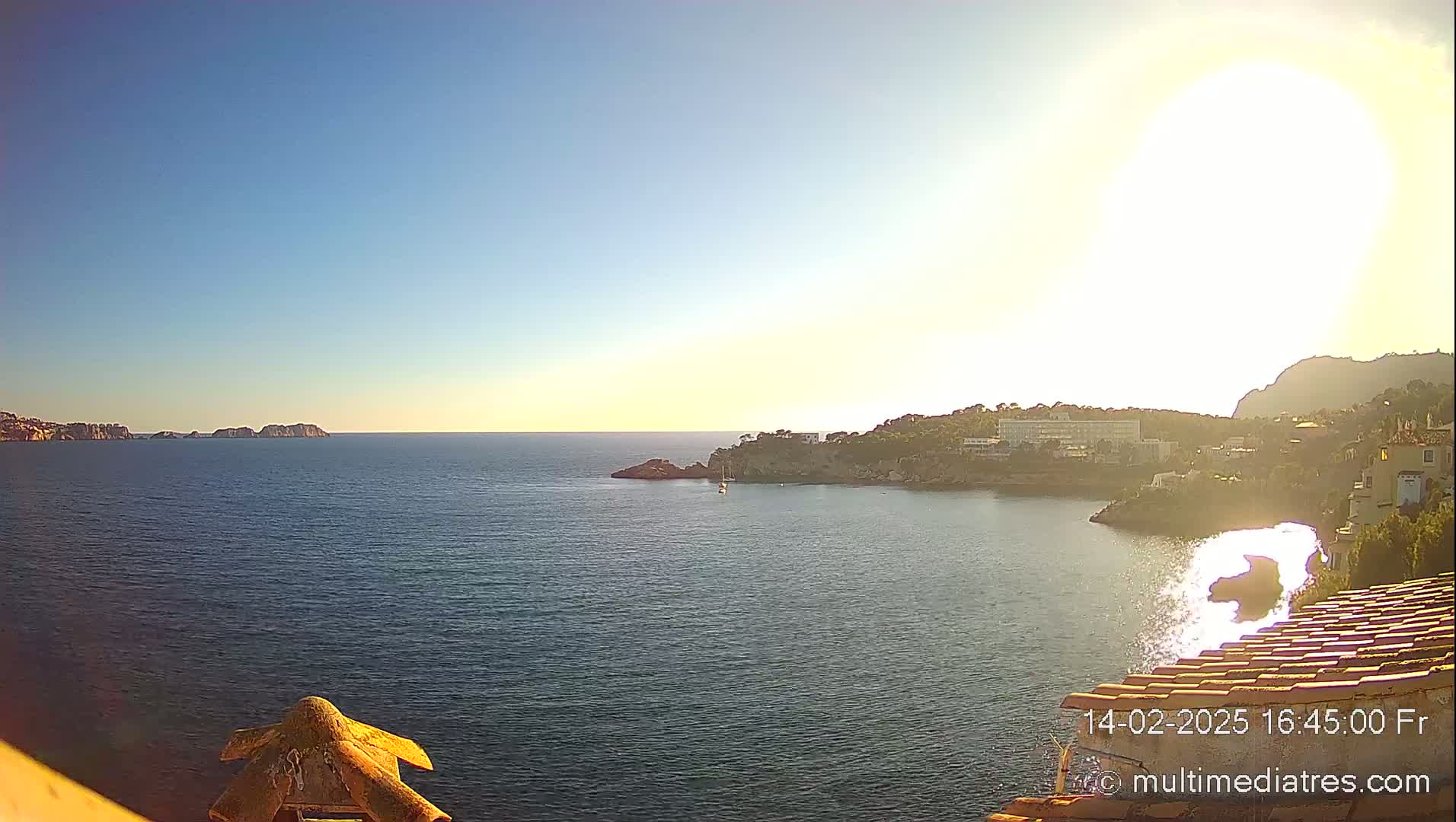 A sunny, clear day overlooks a calm bay with a coastline of buildings and trees, and distant islands visible across the water.
