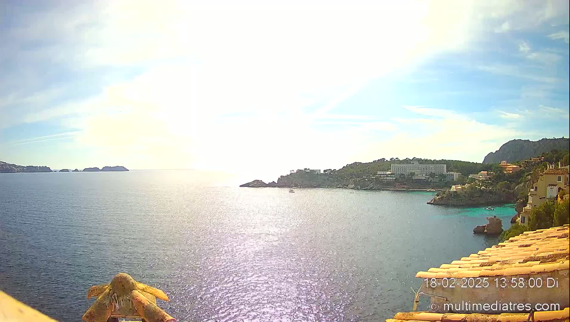 A sunny, partly cloudy day reveals a tranquil coastal scene with a calm sea, distant islands, and buildings nestled along a rocky shoreline.