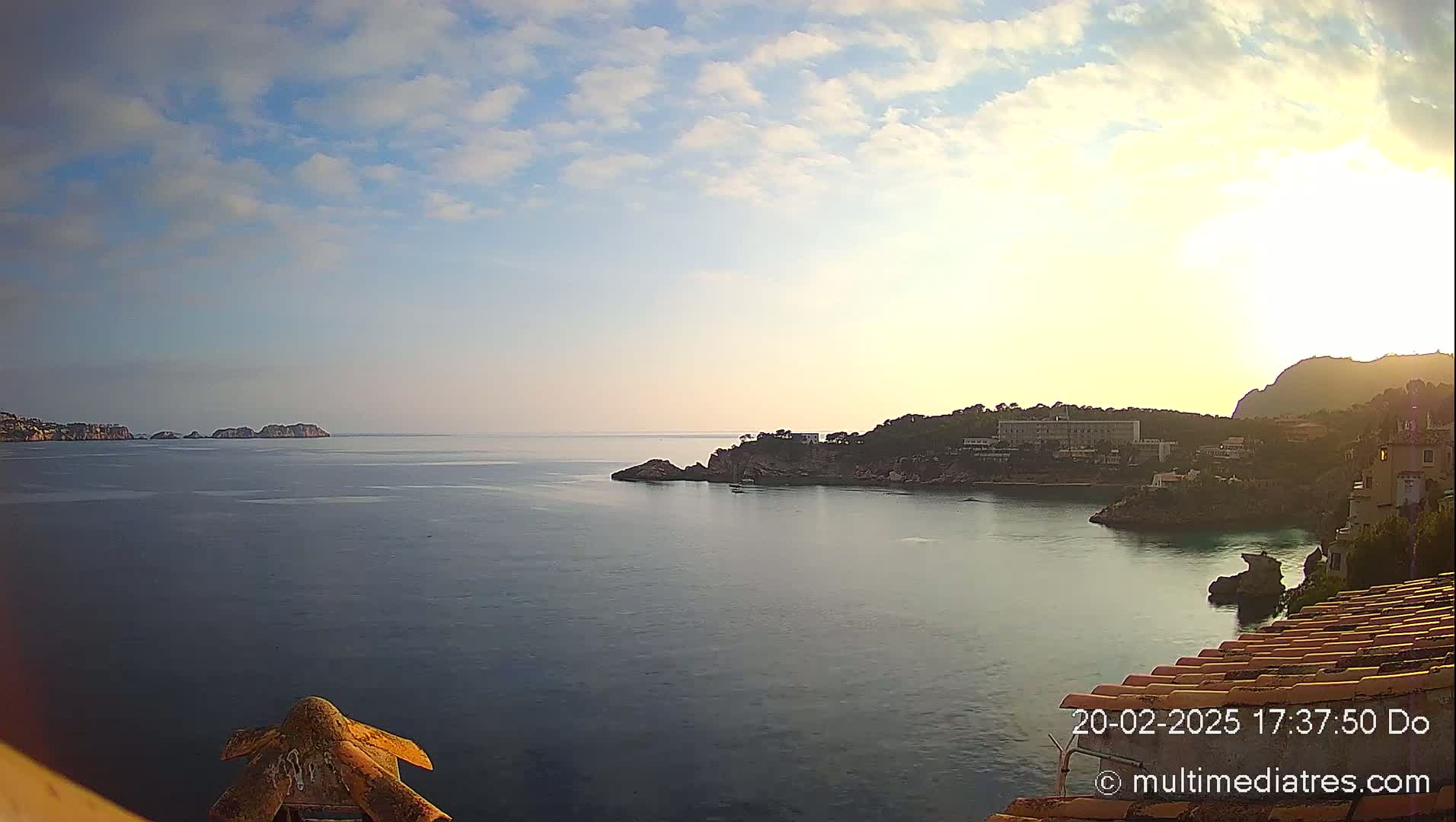 A calm sea stretches out under a partly cloudy sky, with rocky coastline and buildings visible in the mid-ground.
