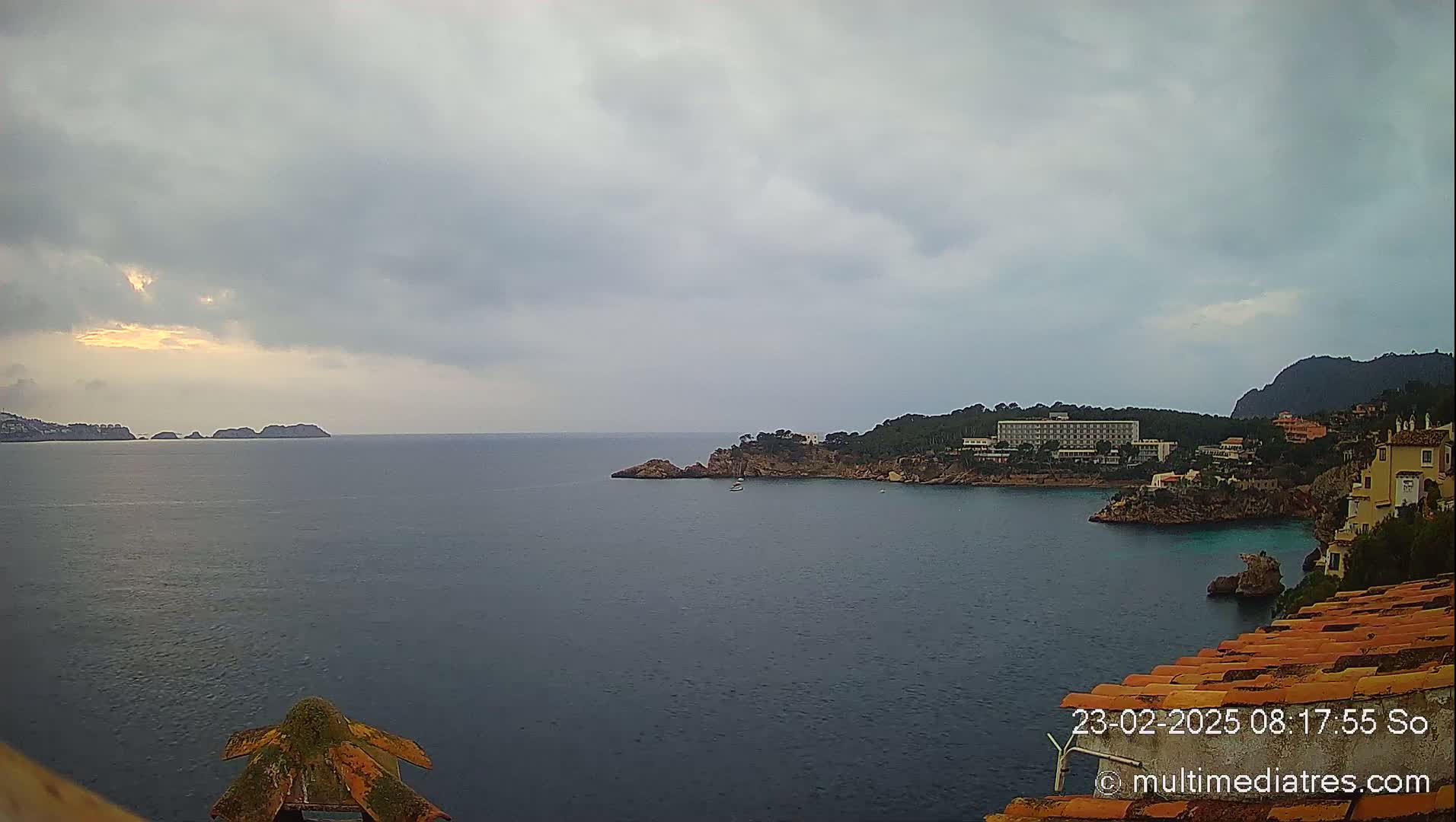 A coastal view on an overcast day shows a calm sea with a distant shoreline, islands, and buildings along a rocky coast.