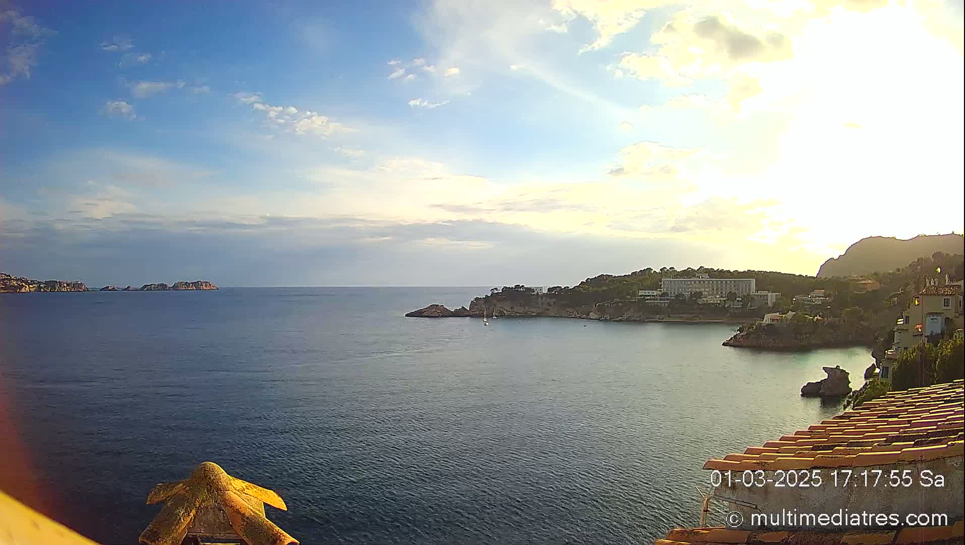 A partly cloudy late afternoon overlooks a calm sea with islands and a coastal town visible in the distance.