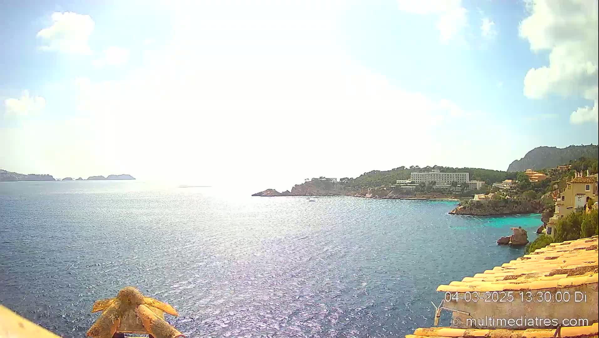 A sunny day overlooking a calm sea with a coastal town and distant islands visible from a high vantage point.