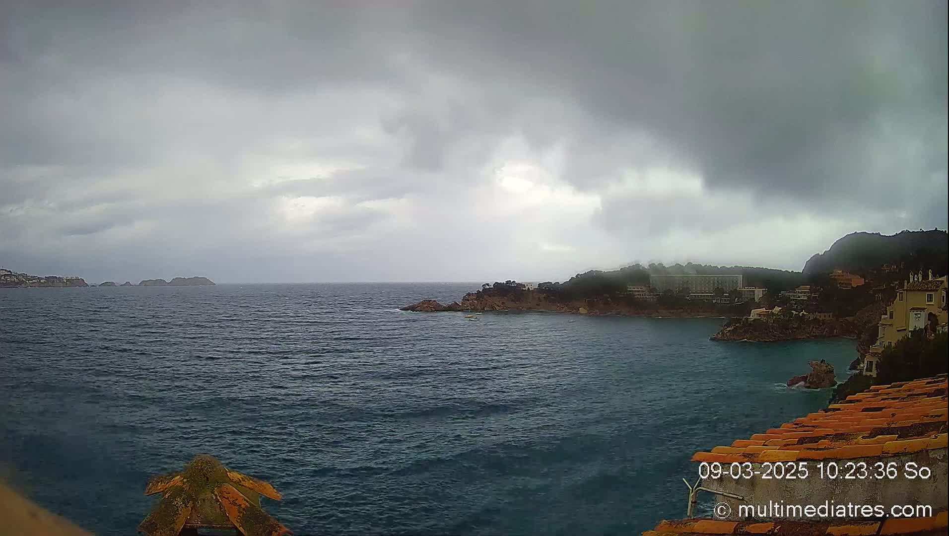 A dark, overcast sky hangs over a choppy sea, partially obscuring a coastal town nestled between rocky headlands.