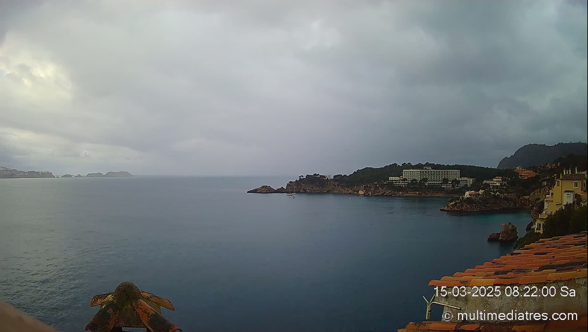 A coastal scene on an overcast day shows a calm body of water with a rocky shoreline featuring buildings and trees.