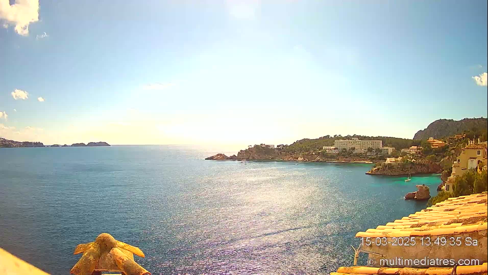 A sunny, clear day overlooking a calm blue ocean bay with buildings and hills on the shore.