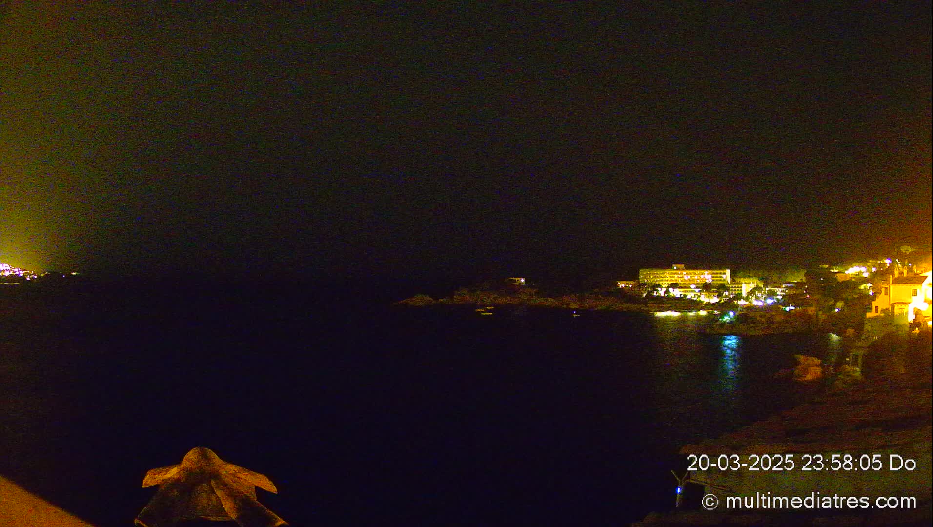 A nighttime view of a dark body of water with a brightly lit coastline across it.