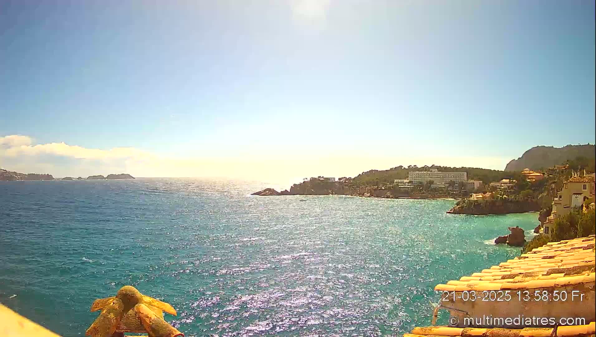 A sunny day overlooking a sparkling blue ocean bay with a coastal town and rocky outcrops.