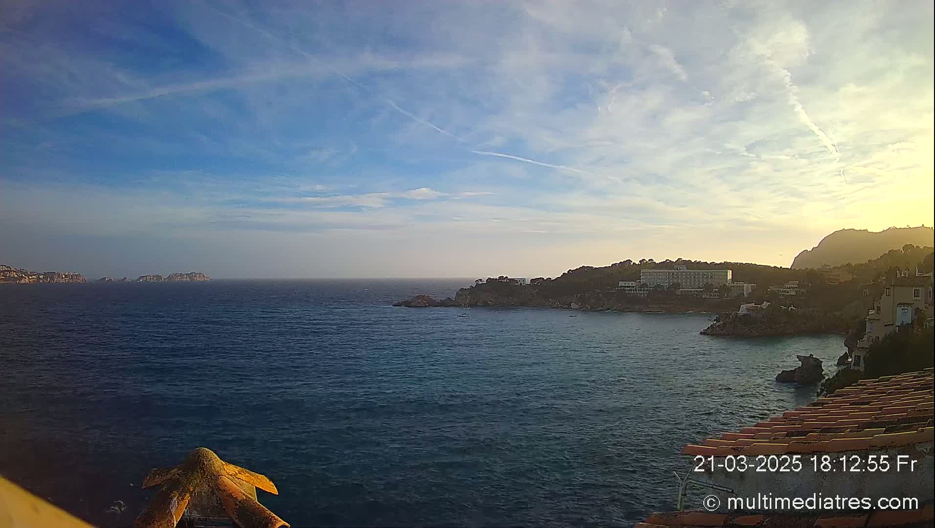 A calm sea stretches out to a distant coastline under a partly cloudy sky with hints of sunset.