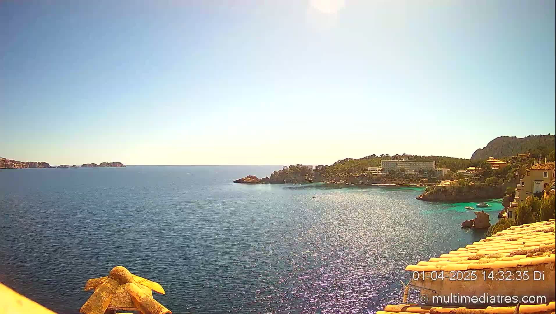 A sunny day reveals a tranquil ocean scene with a coastline featuring buildings, vegetation, and rocky outcrops.