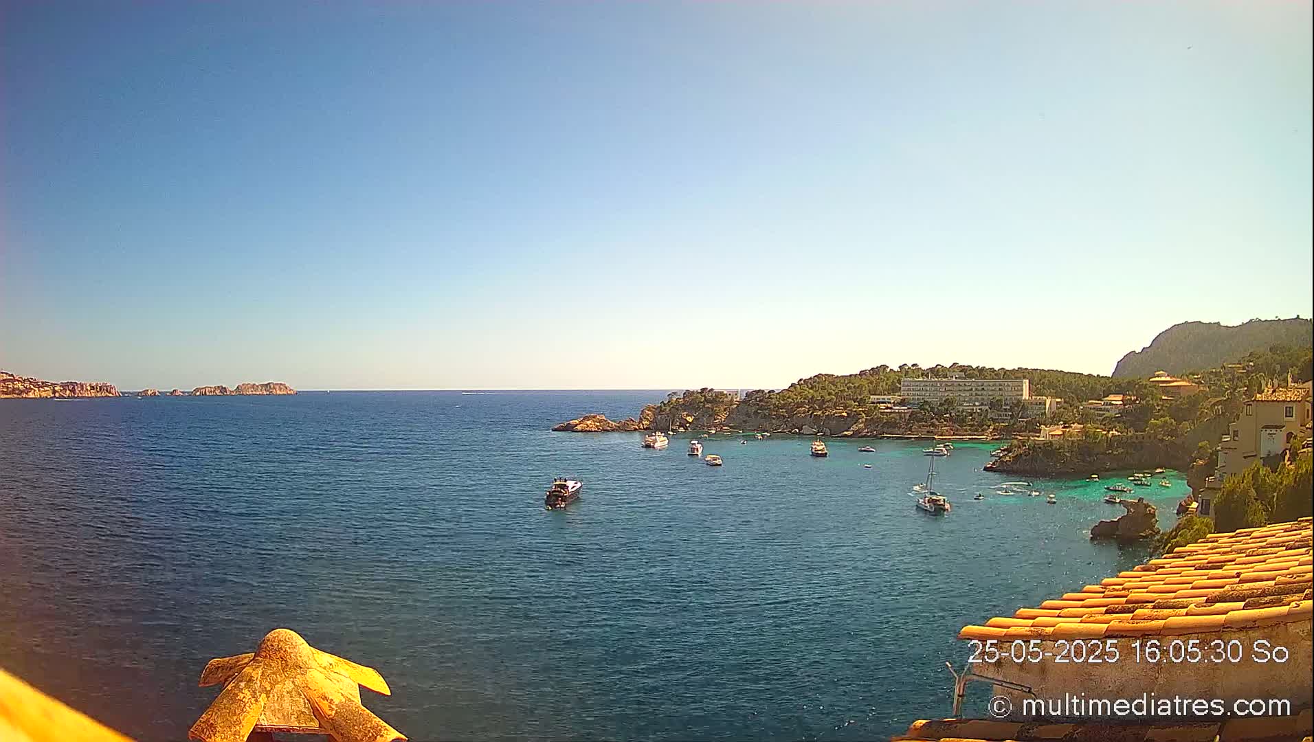 A tranquil bay with several boats is seen from a high vantage point on a clear, sunny day.