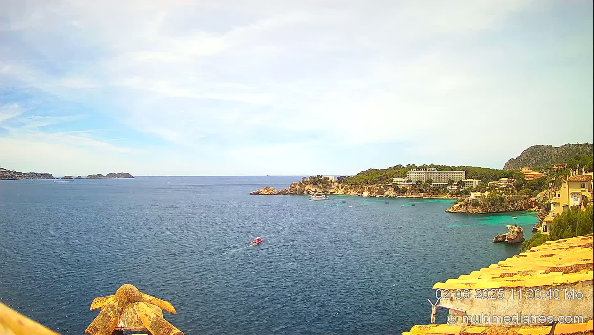 A partly sunny day overlooks a calm, blue ocean bay with a coastline featuring hotels, homes, and rocky cliffs.
