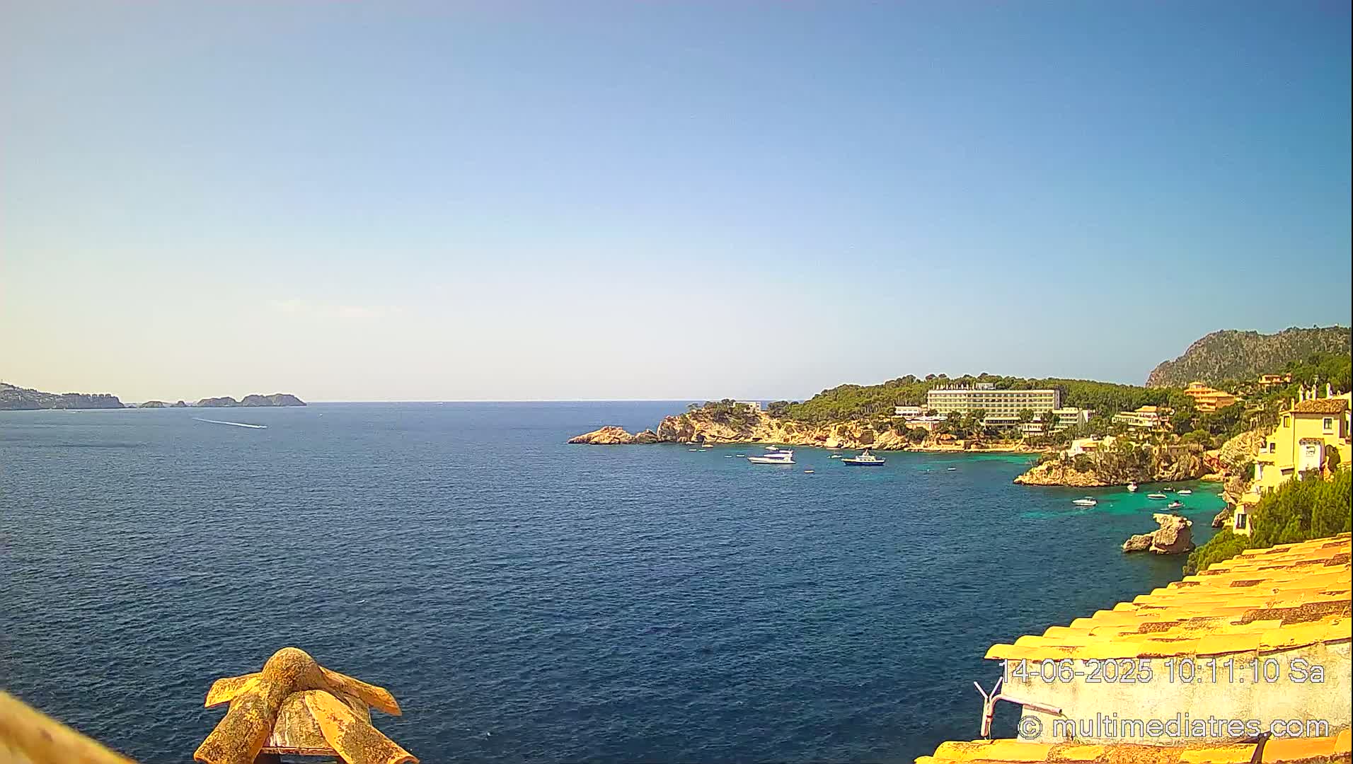 A sunny day overlooking a calm blue sea with a coastal town,  boats, and rocky cliffs.
