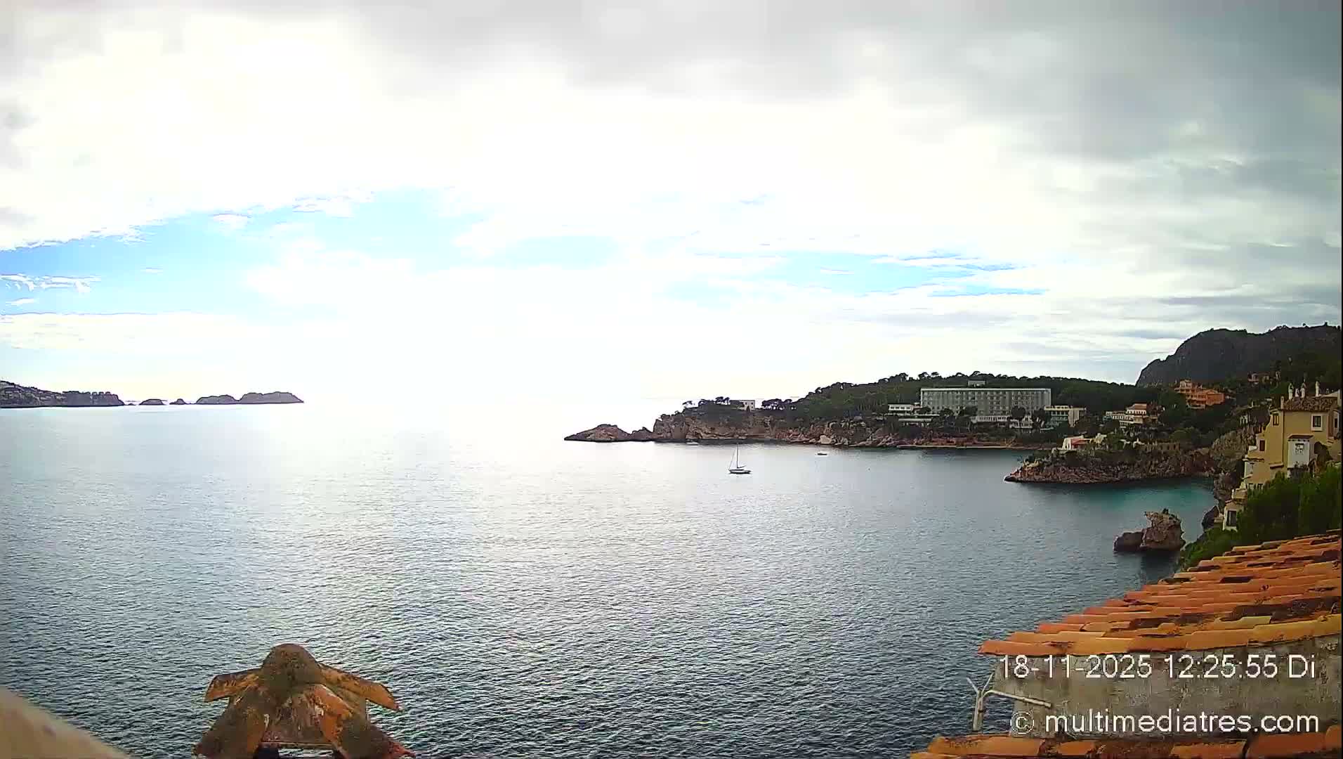 A clear, starry night sky hangs over a dark bay reflecting the lights of illuminated coastal buildings, with a few small boats visible on the calm water.