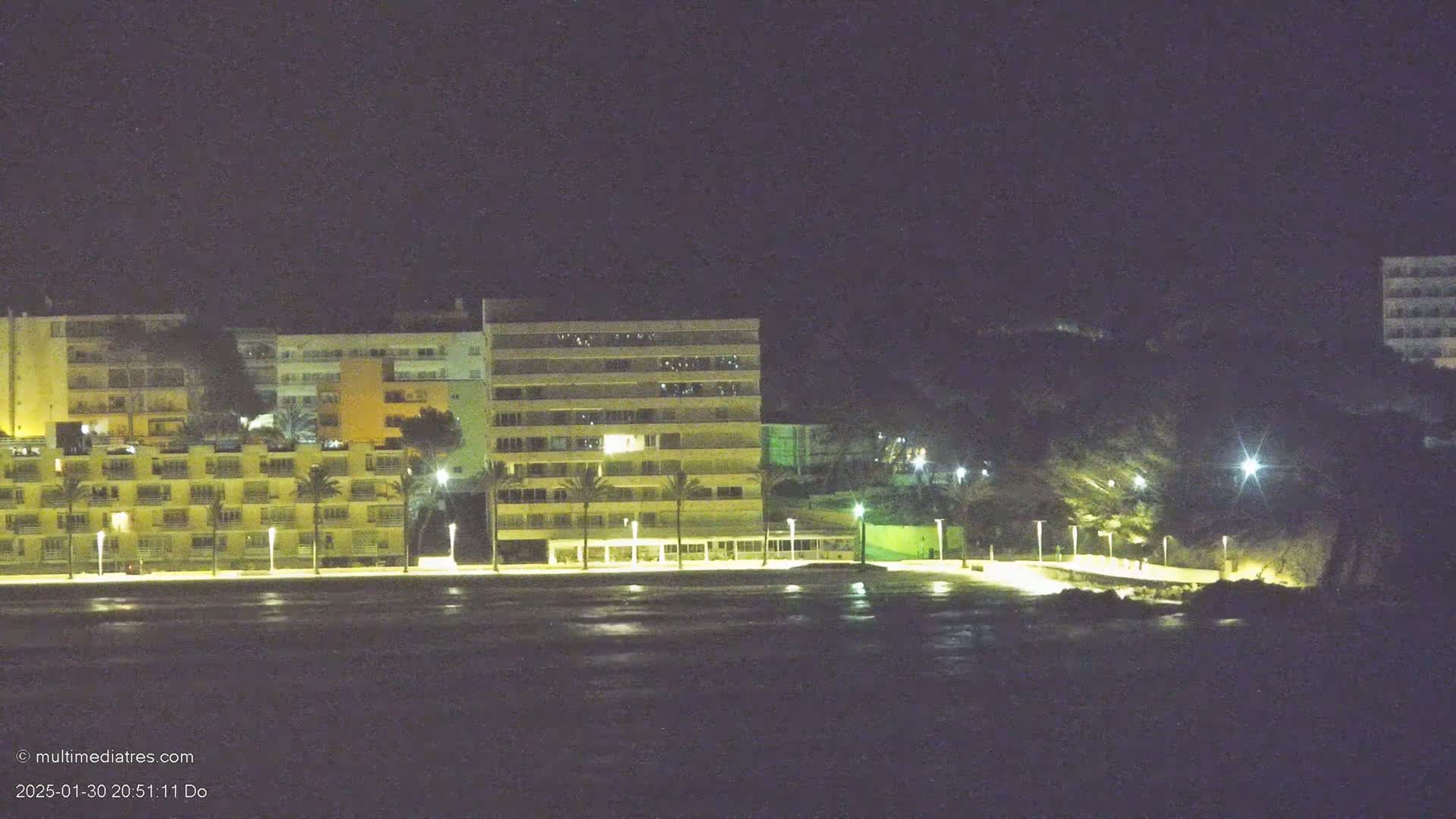 Lit-up apartment buildings line a dark beach at night.