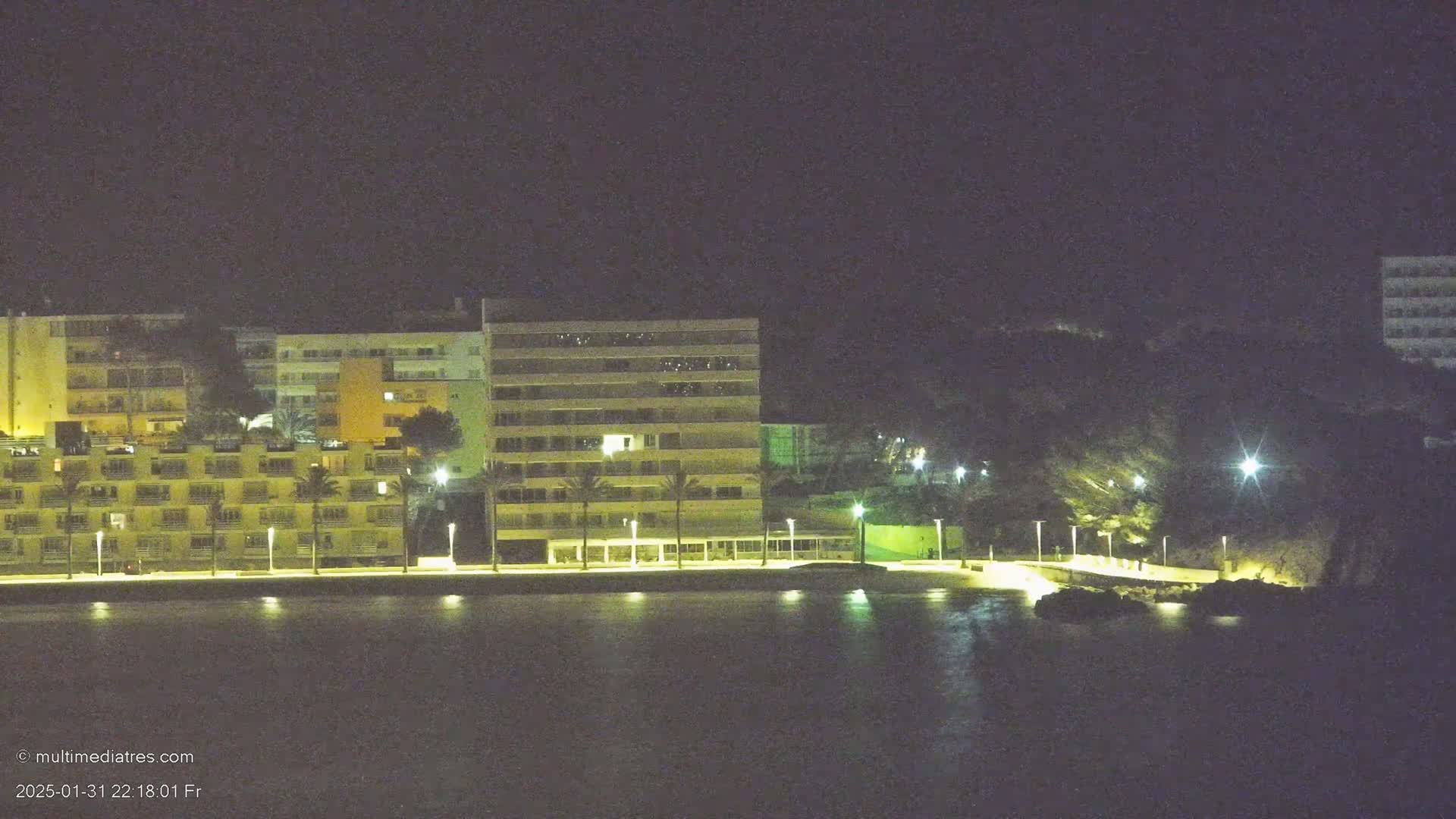 A line of illuminated buildings sits along a dark waterfront at night.