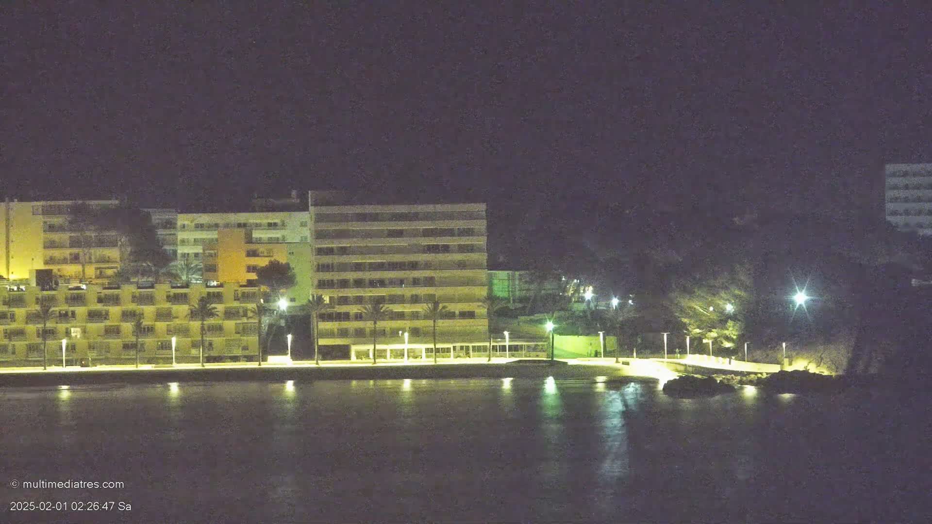 A row of illuminated buildings sits along a dark waterfront at night.