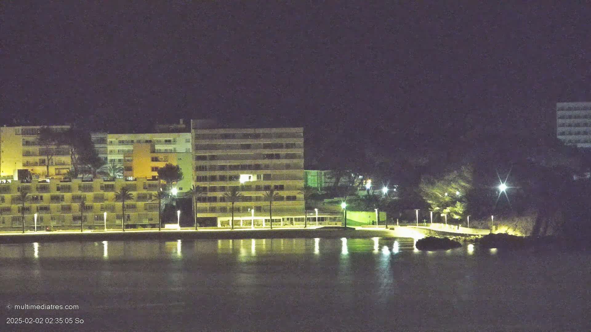 Illuminated apartment buildings line a calm, dark waterfront at night.