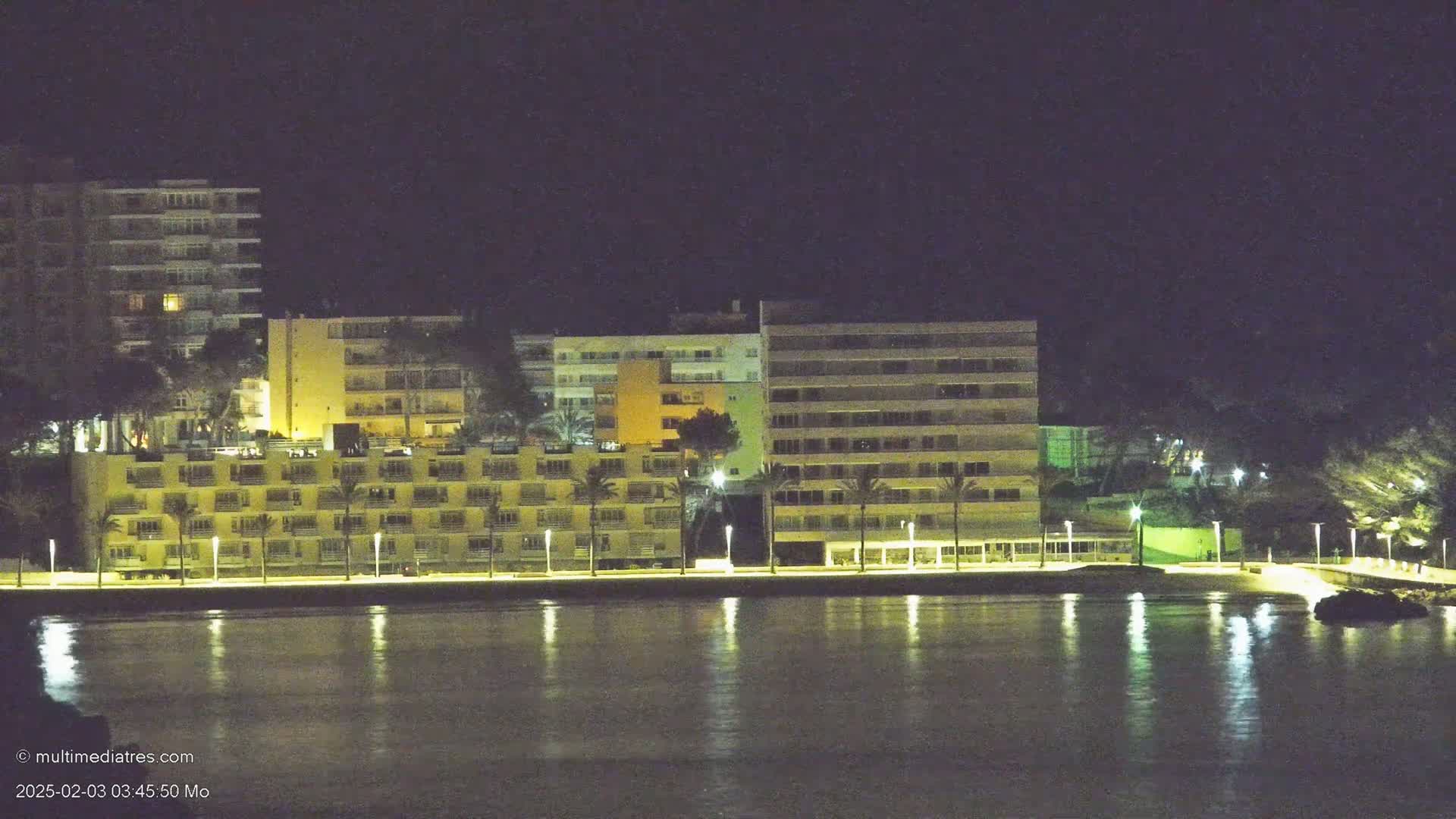 Illuminated multi-story buildings line a calm, dark waterfront at night.