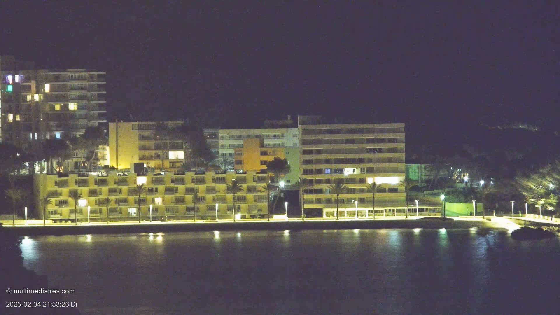 A line of illuminated buildings sits beside a calm body of water at night.