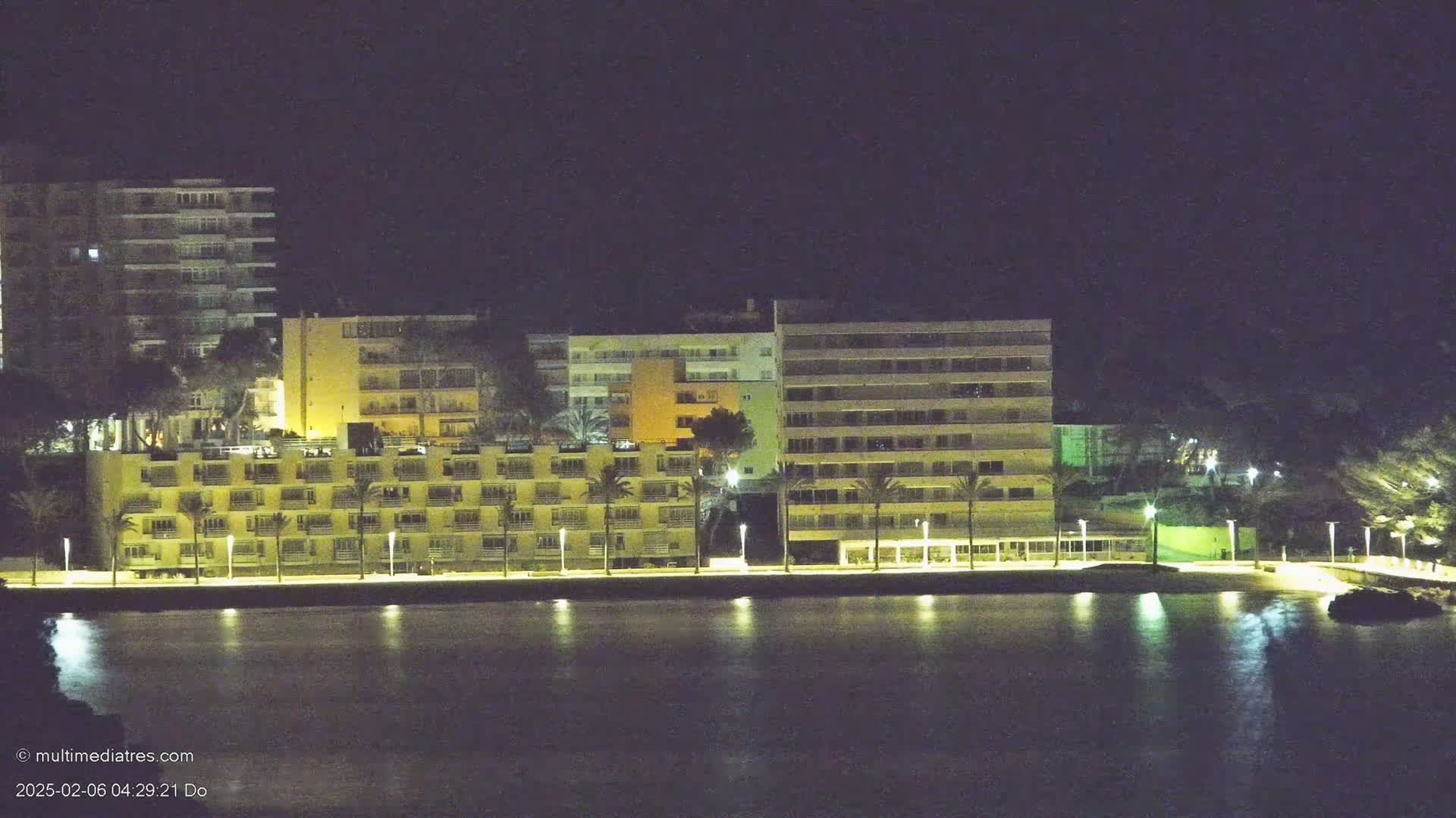 Lit-up multi-story buildings line a waterfront at night.