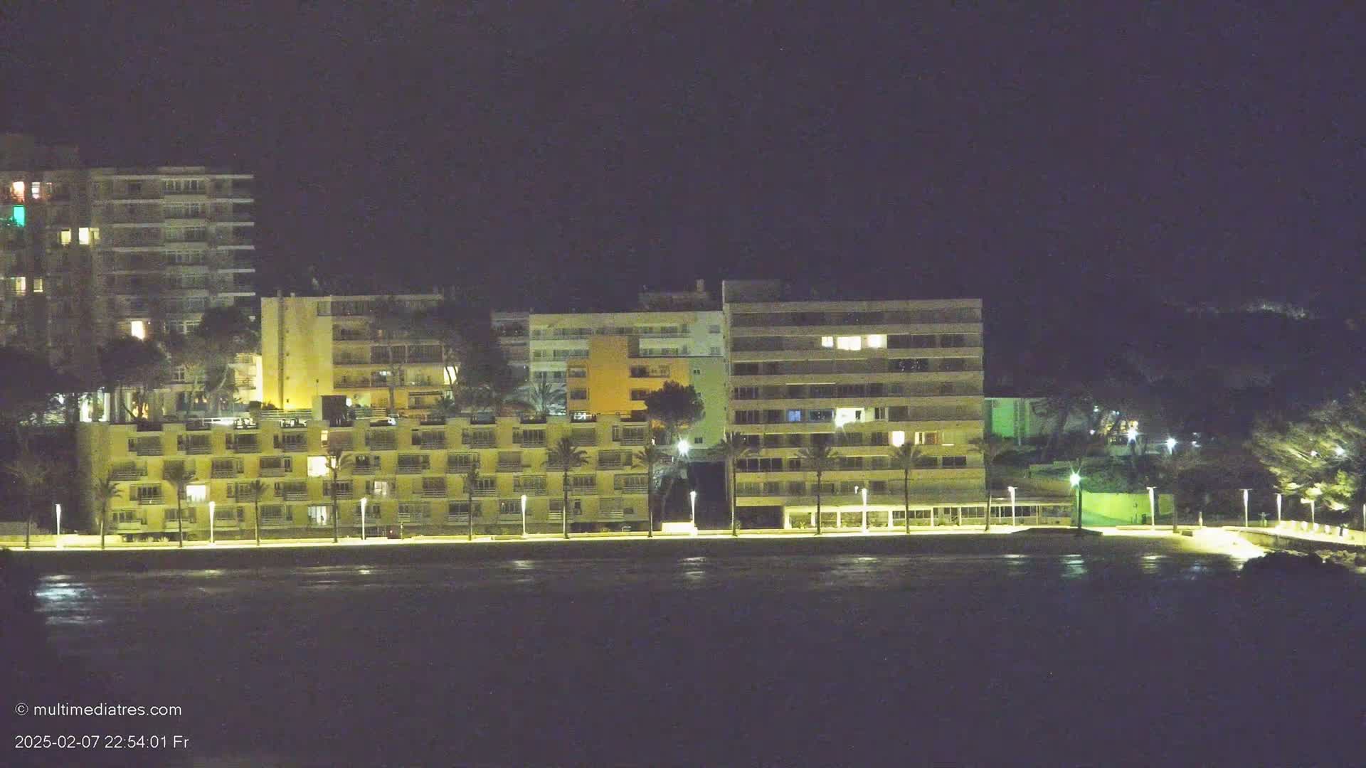 Illuminated multi-story buildings line a waterfront at night.