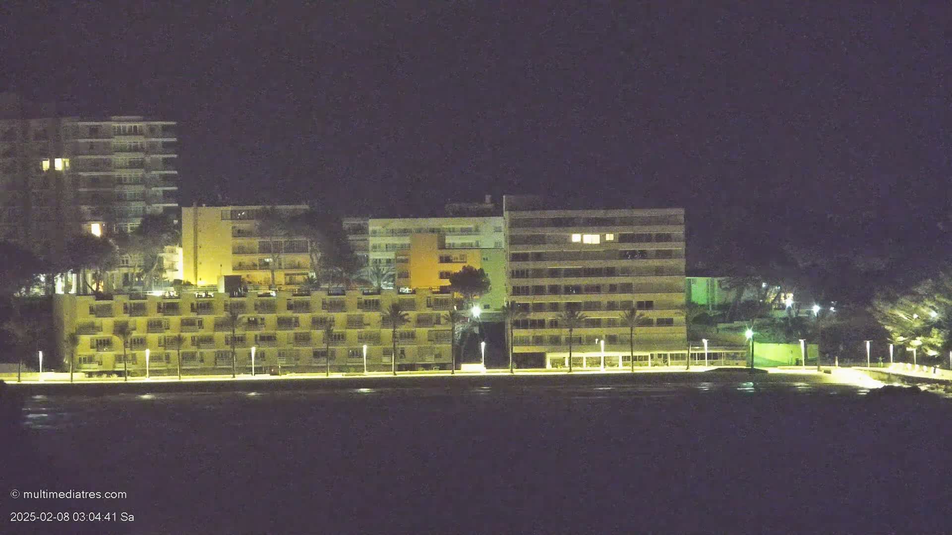 Illuminated apartment buildings line a waterfront at night.