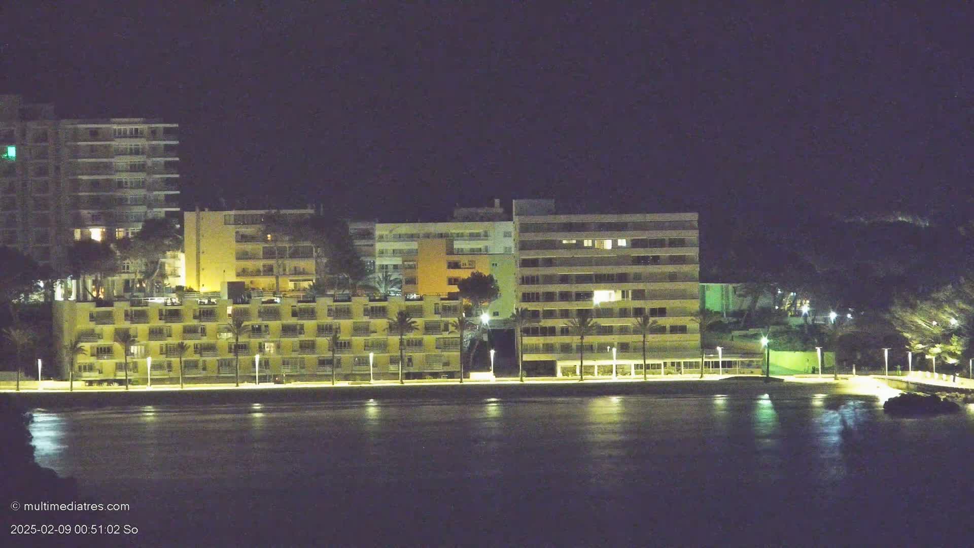 A row of illuminated buildings stands along a dark waterfront at night.