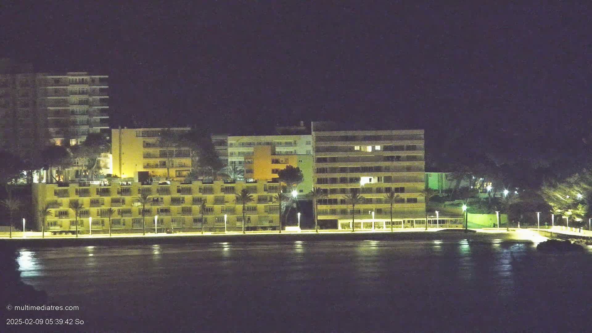 Several multi-story buildings illuminated at night line a calm body of water.