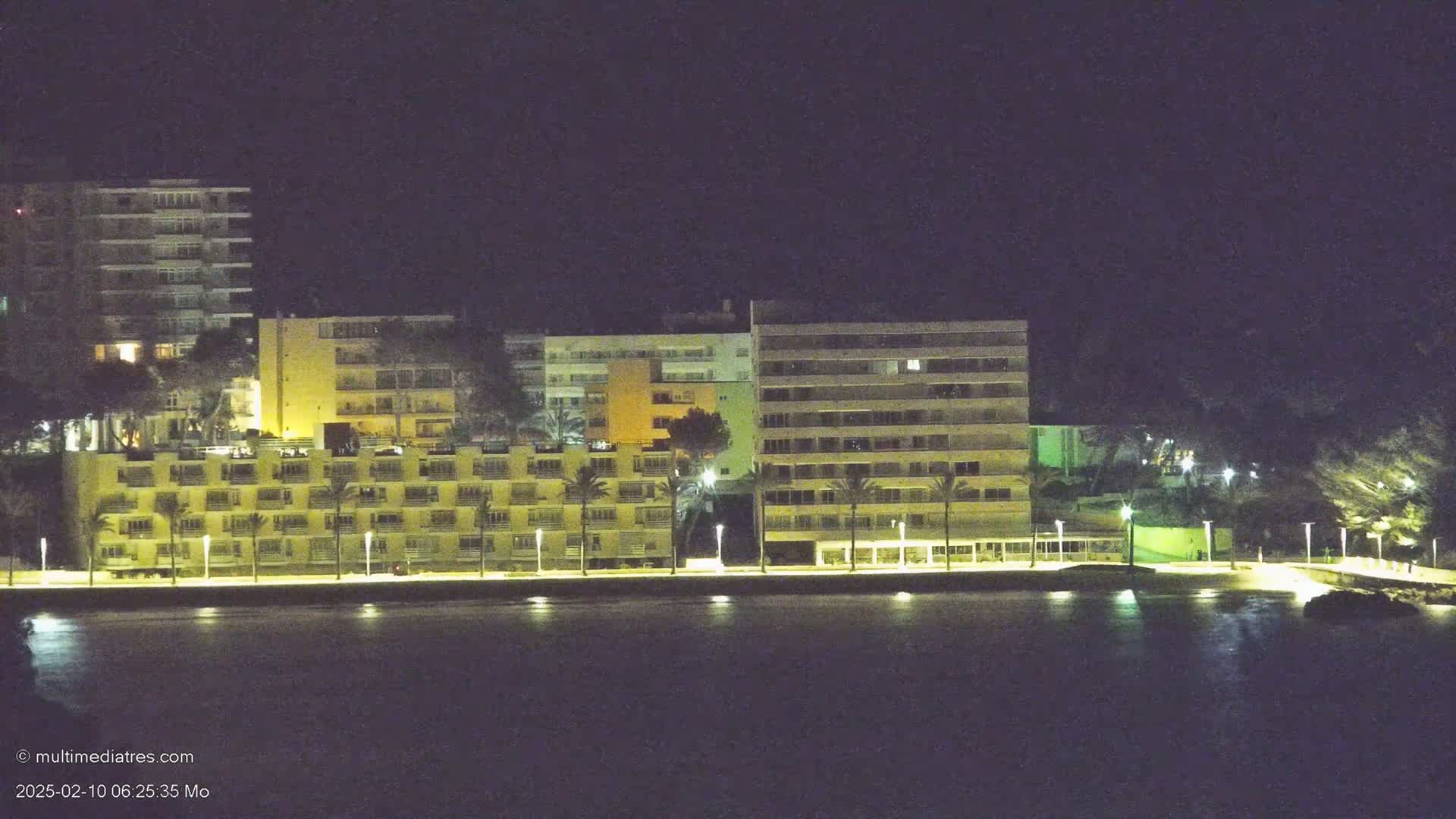 A row of illuminated beachfront buildings is seen at night across a dark body of water.