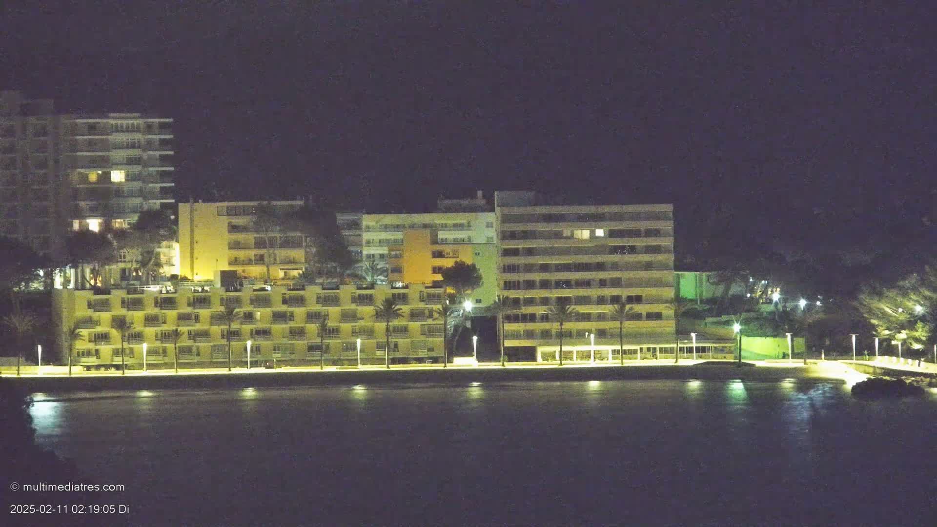 A row of illuminated beachfront hotels and buildings at night, under a dark sky.