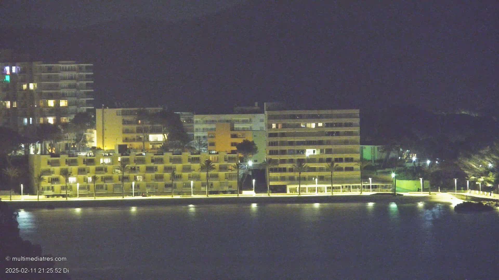 Illuminated multi-story buildings line a waterfront at night under a dark sky.