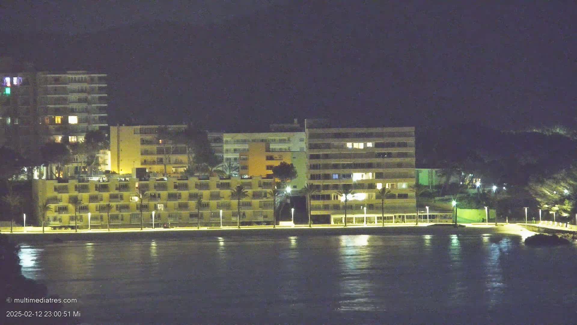 A row of illuminated buildings lines a calm, dark waterfront at night.