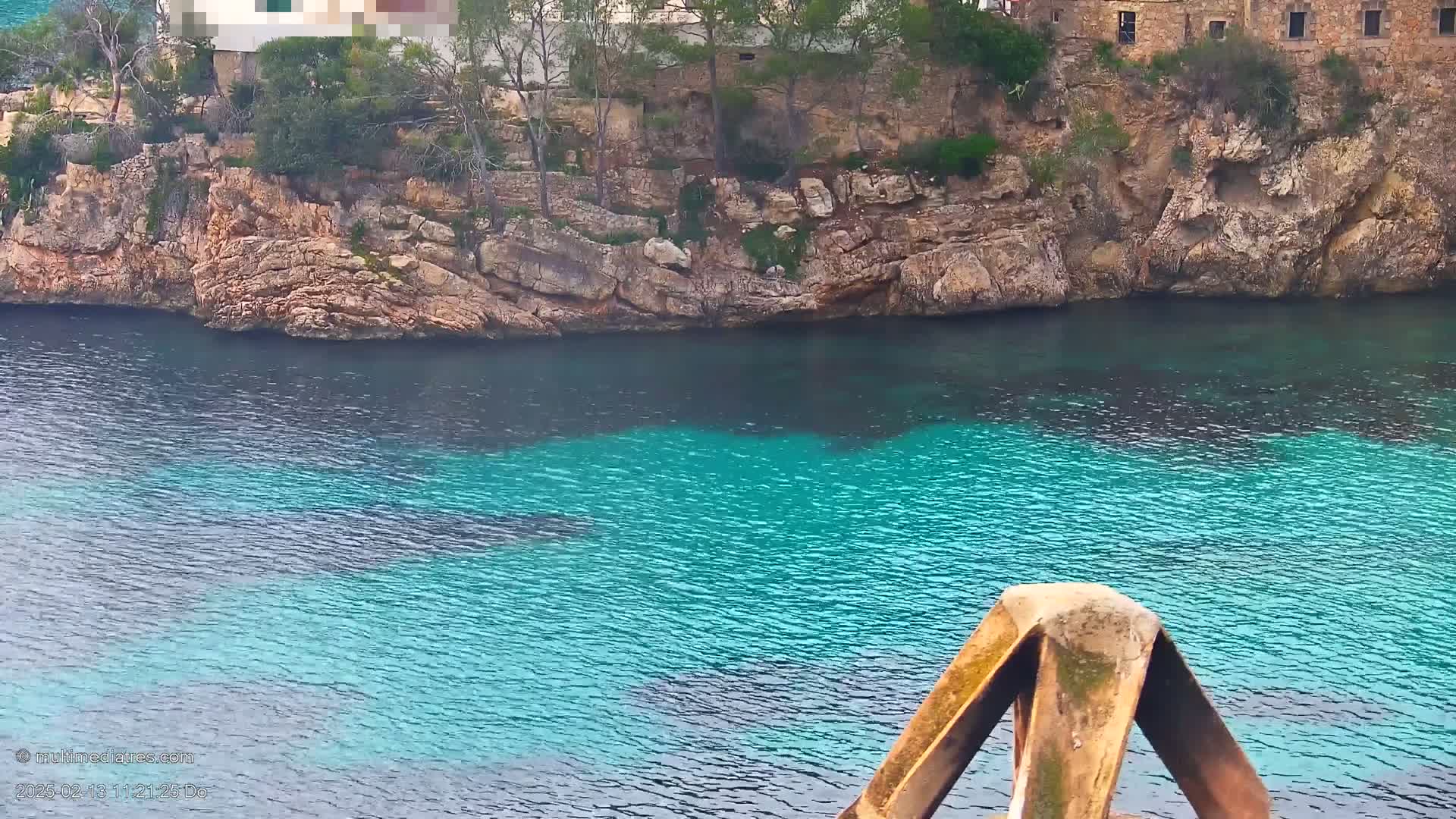 A rocky shoreline with sparse vegetation borders a cove of bright turquoise water.