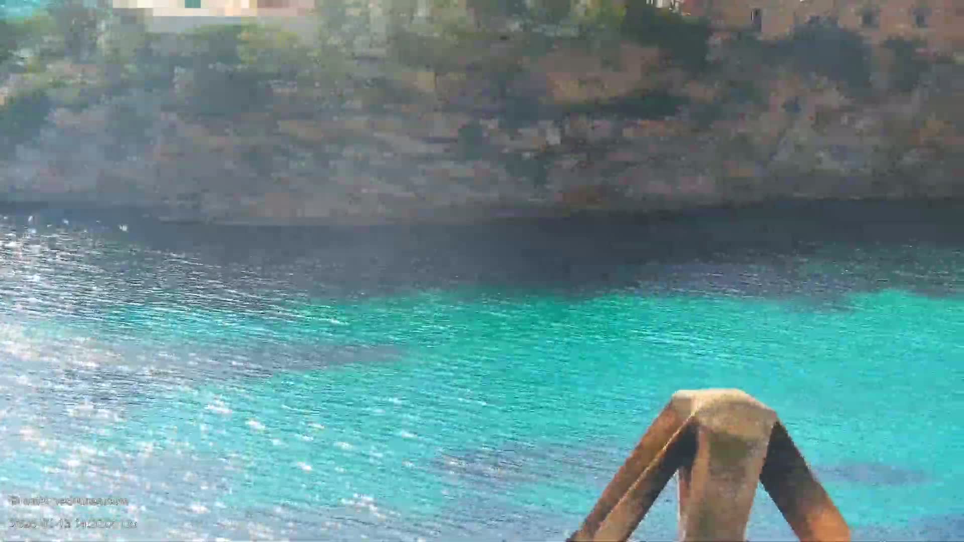Bright turquoise water laps against a rocky shoreline under a sunny sky.