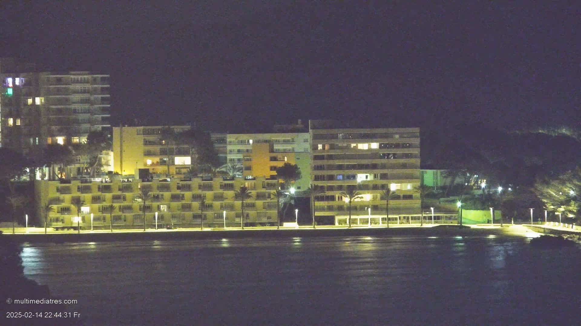 A row of illuminated buildings stands along a dark waterfront at night.
