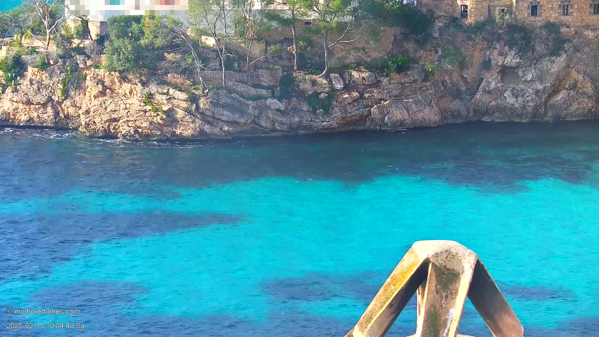 A rocky cliff, dotted with sparse vegetation, overlooks a vibrant turquoise sea.
