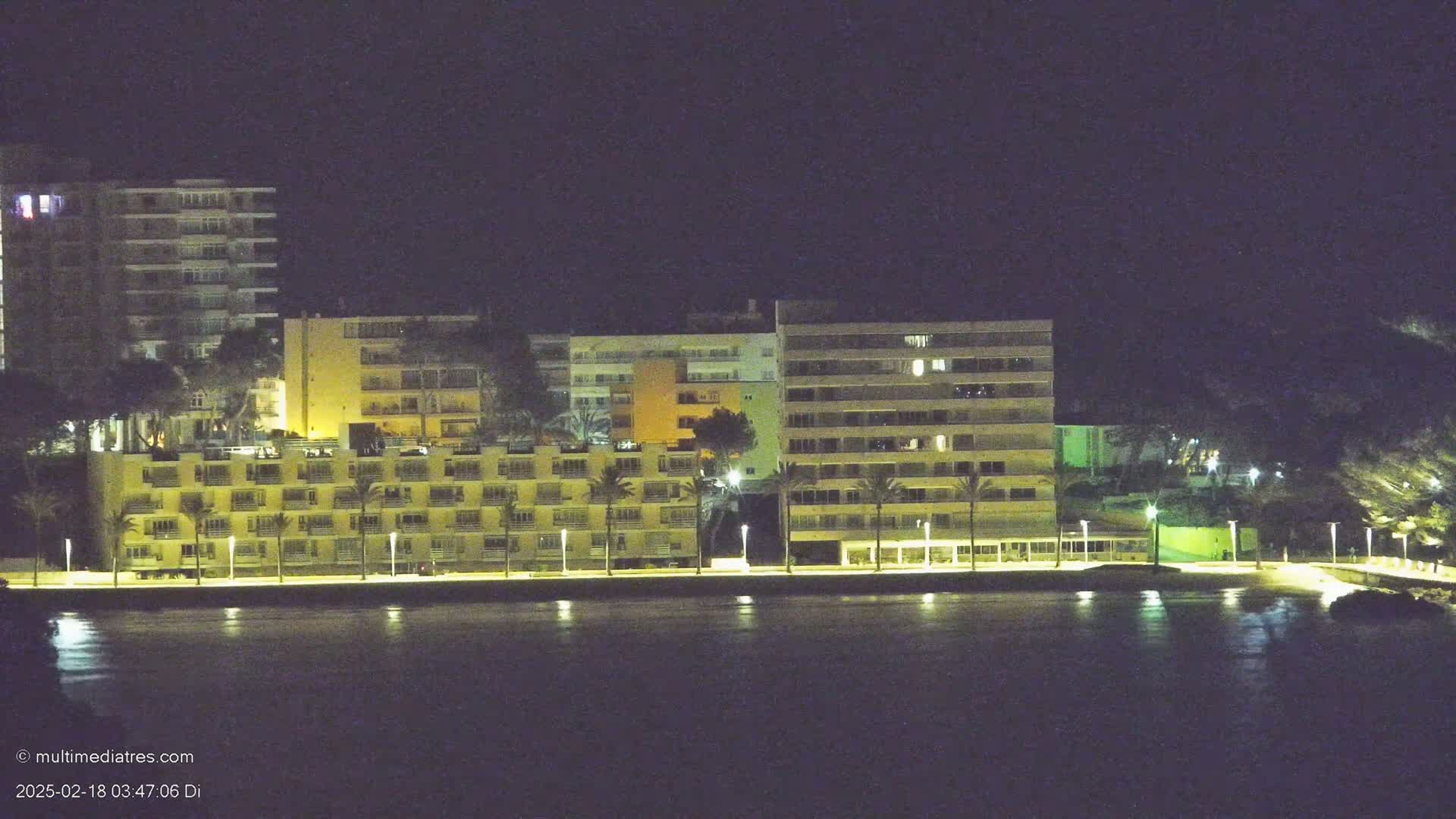 A row of illuminated multi-story buildings lines a dark waterfront at night.