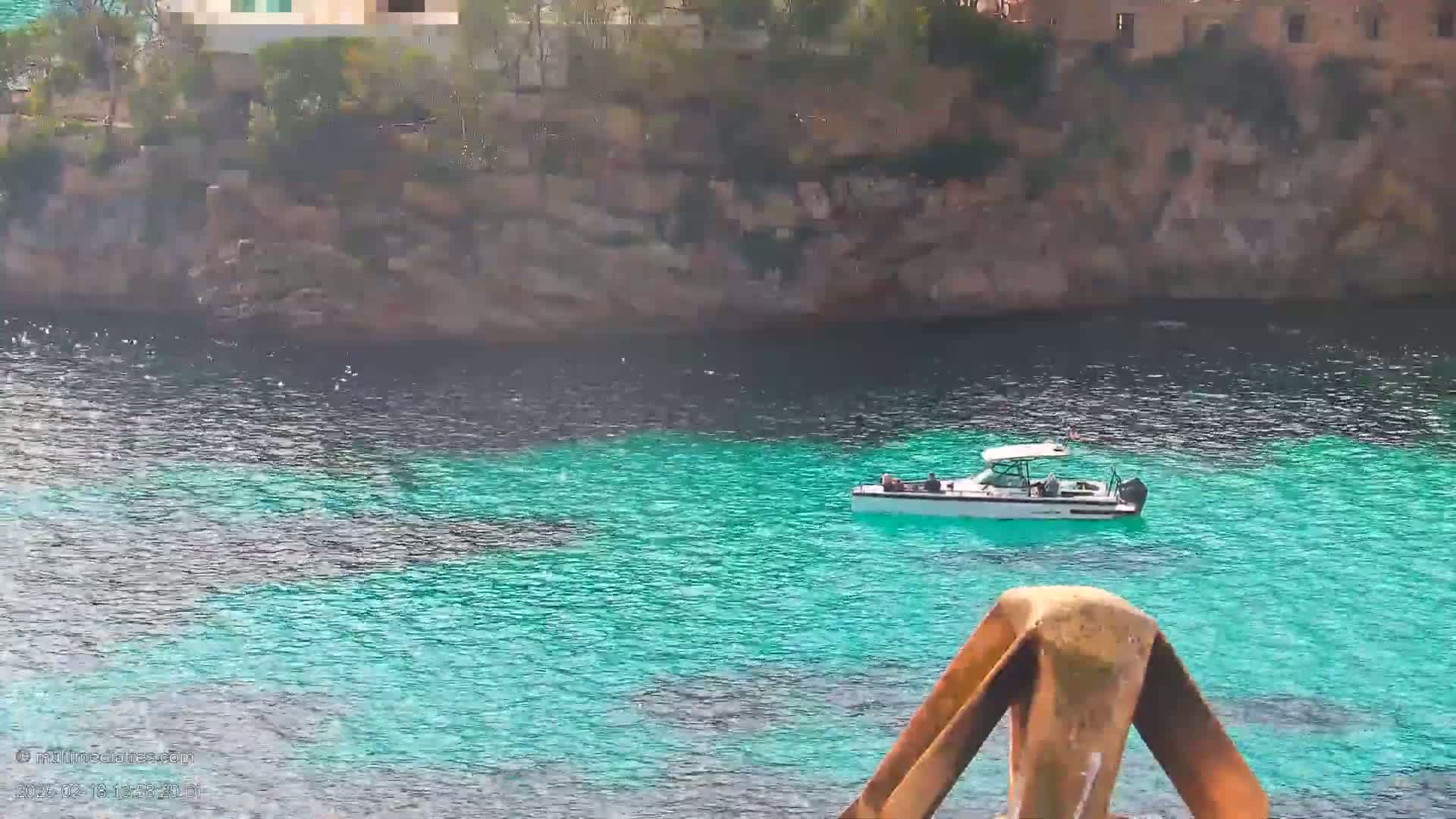 A white boat floats on bright turquoise water near a rocky shore.