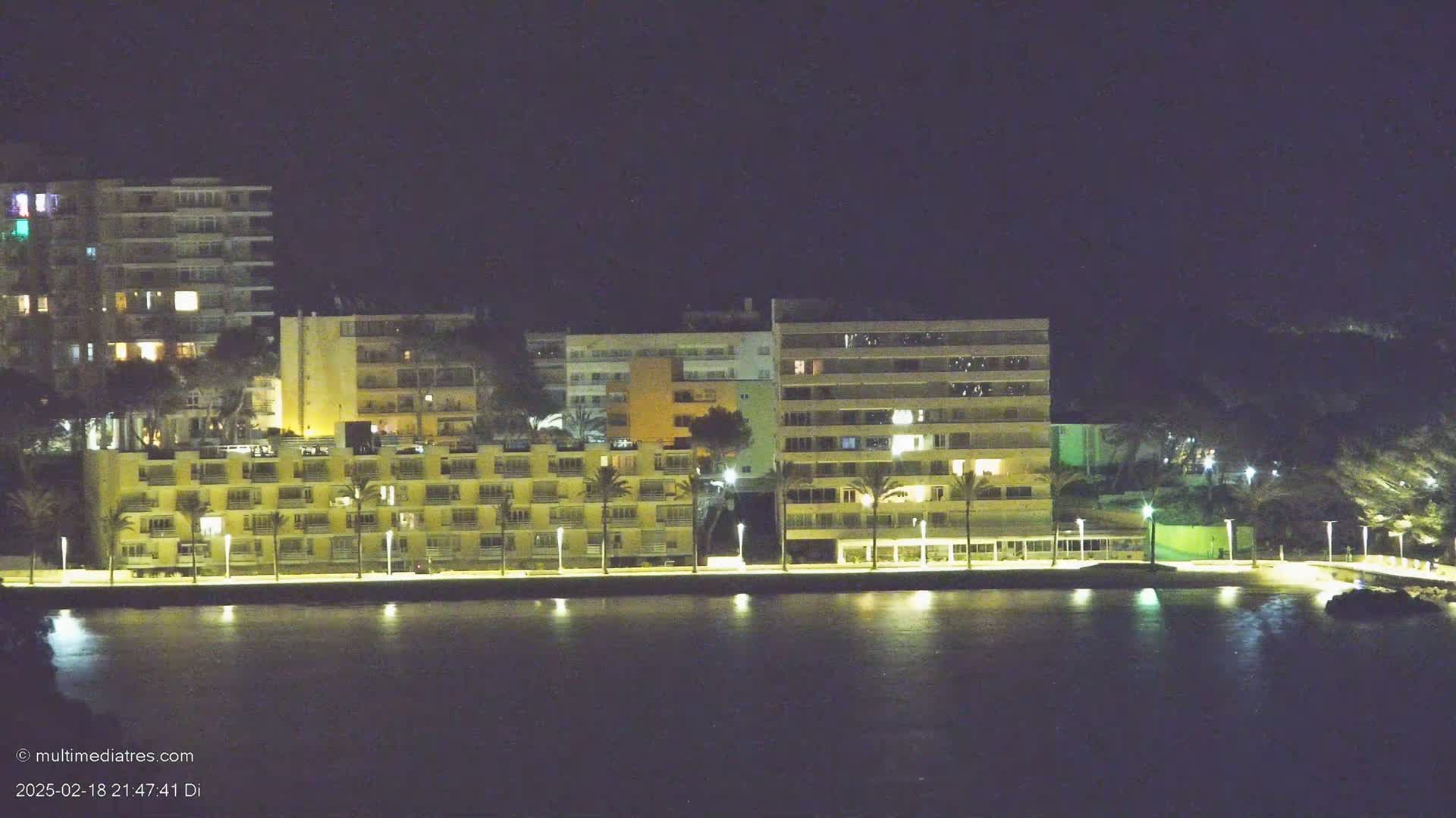 A row of illuminated buildings stands along a calm body of water at night.