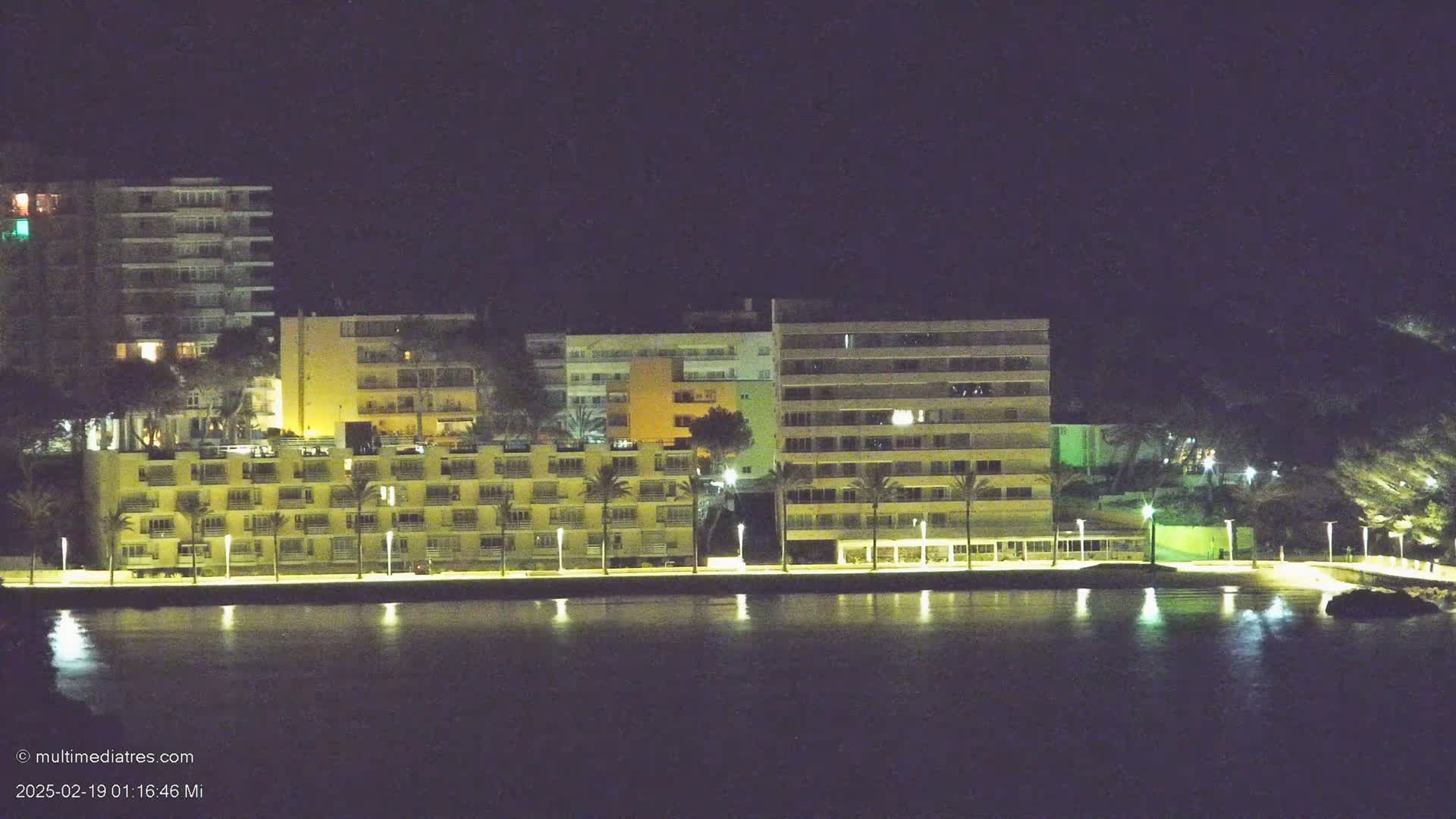 A row of illuminated buildings stands along a dark waterfront at night.