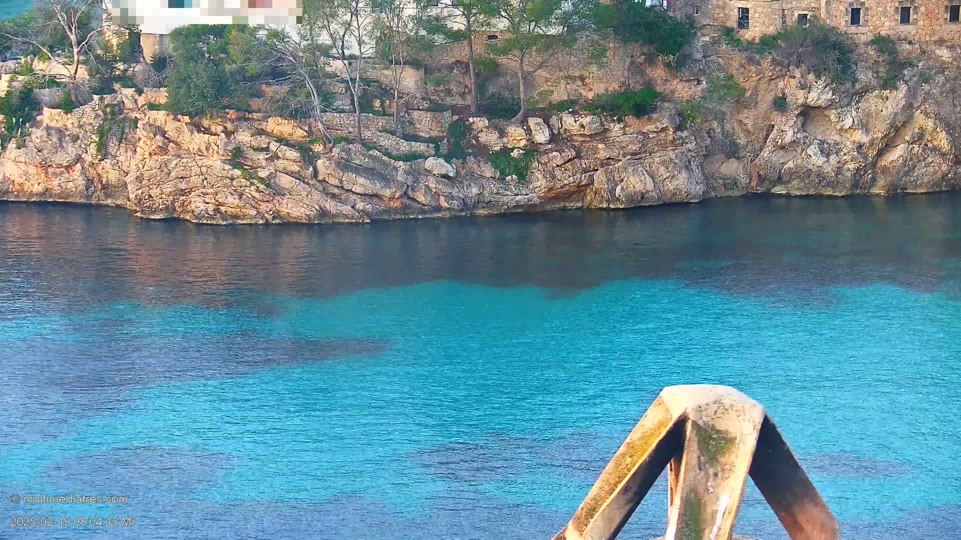 A rocky cliff overlooking a calm, vibrant turquoise body of water.