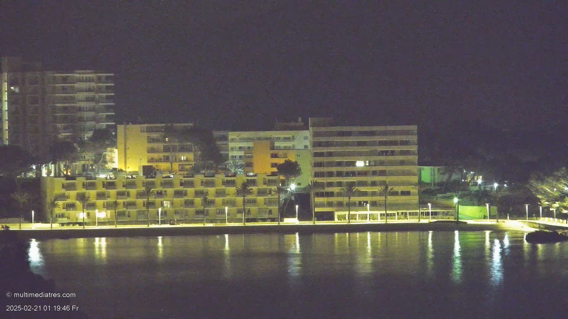 A row of illuminated buildings stands along a calm body of water at night.